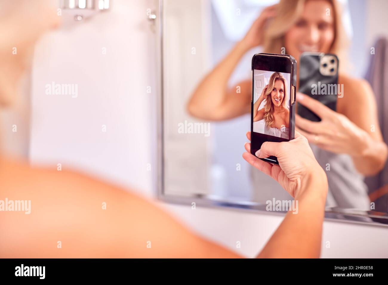 Mujer madura Preparándose en el cuarto de baño en casa posando para Selfie en el teléfono móvil Foto de stock