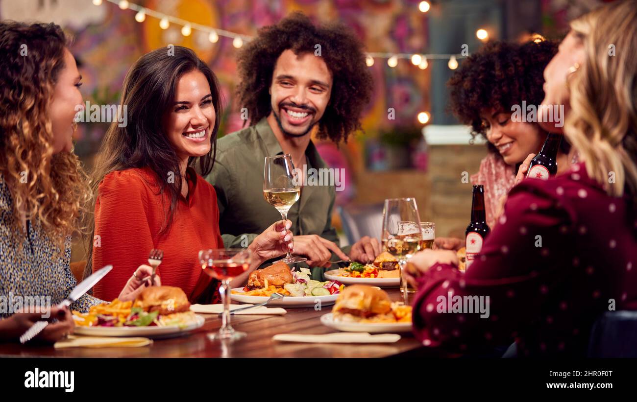 Grupo multicultural de amigos disfrutando de la comida nocturna y beber en el restaurante juntos Foto de stock