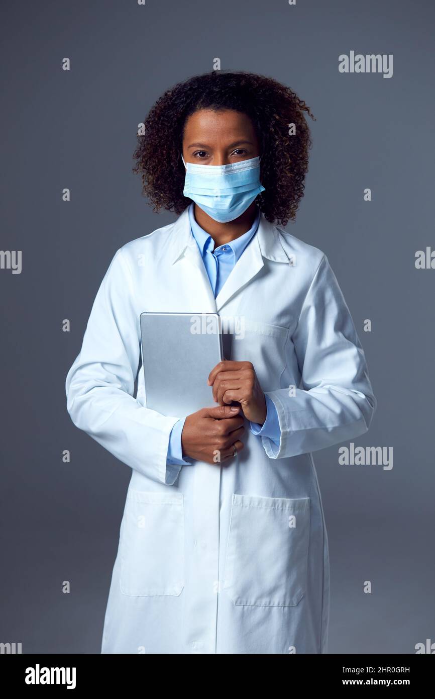 Estudio Retrato de la doctora en el abrigo de laboratorio con máscara de la cara que sostiene la tableta digital Foto de stock