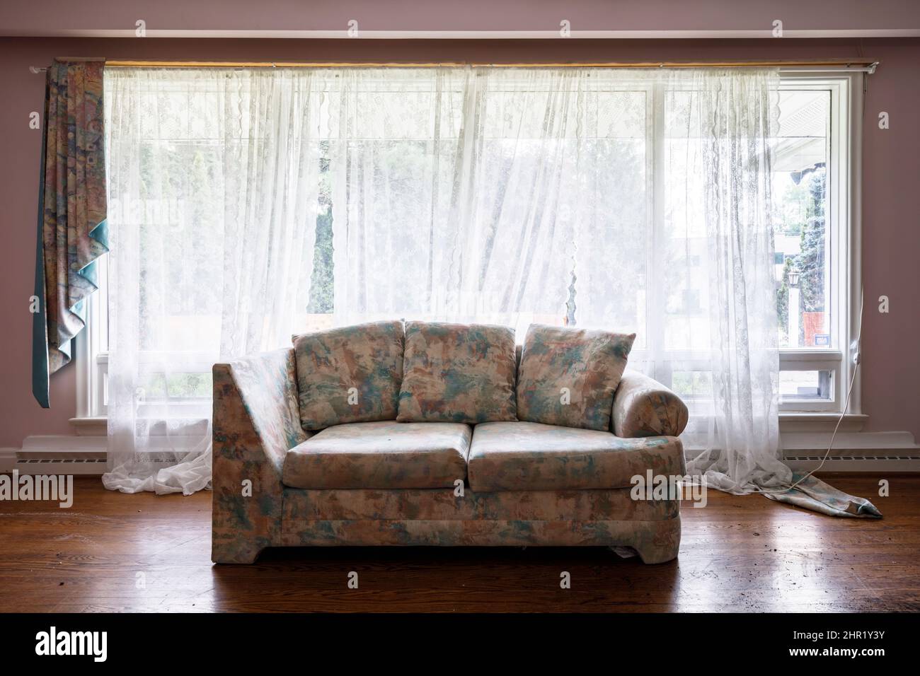 Un sofá feo dentro de una habitación vacía frente a una ventana. Esta casa ha sido demolida. Foto de stock