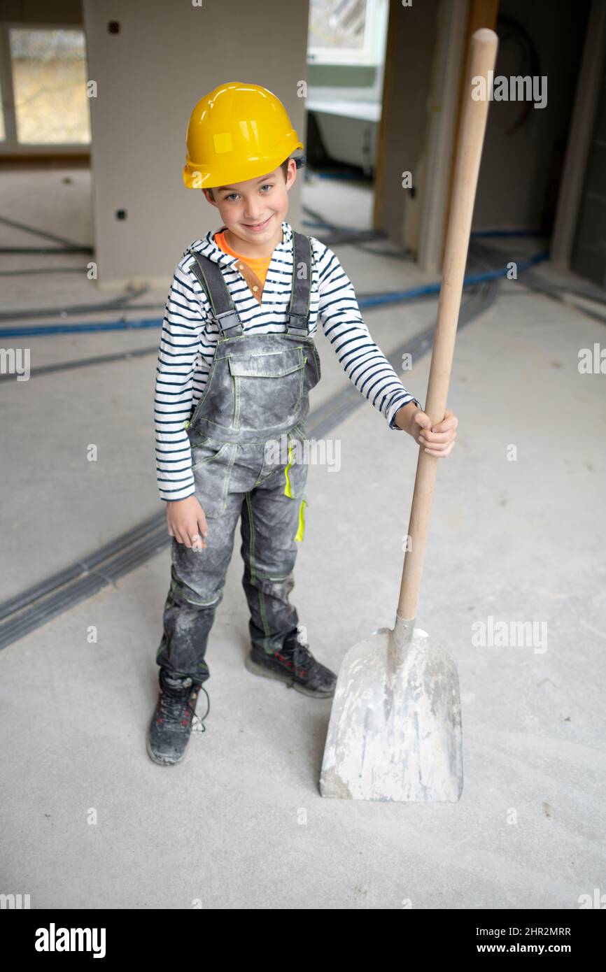 niño frío de seguridad amarillo y peto en el sitio de construcción en una casa y con pala en mano Fotografía de stock - Alamy