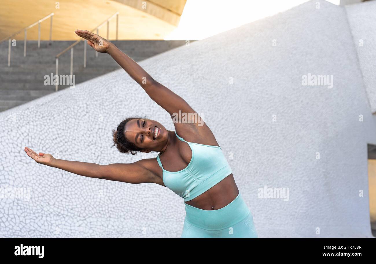 Mujer africana joven que hace estiramientos antes de la sesión de entrenamiento en la ciudad - El concepto del estilo de vida de la gente del deporte Foto de stock