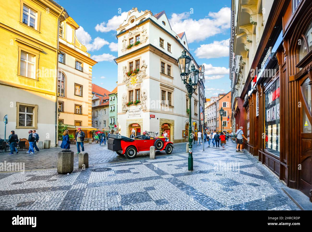 Los turistas paseos turísticos, ir de compras y disfrutar de los cafés mientras pasan por un automóvil rojo vintage en una pintoresca sección de la Ciudad Vieja de Praga, República Checa. Foto de stock