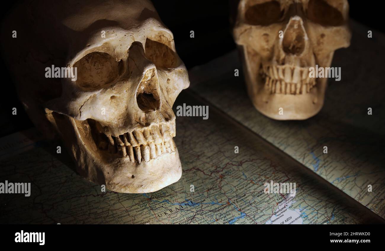 Dos cráneos opuestos que representan la guerra o el conflicto de Rusia y Ucrania. La palabra Ucrania es prominente en un mapa oscurecido de la región de tensión. Foto de stock