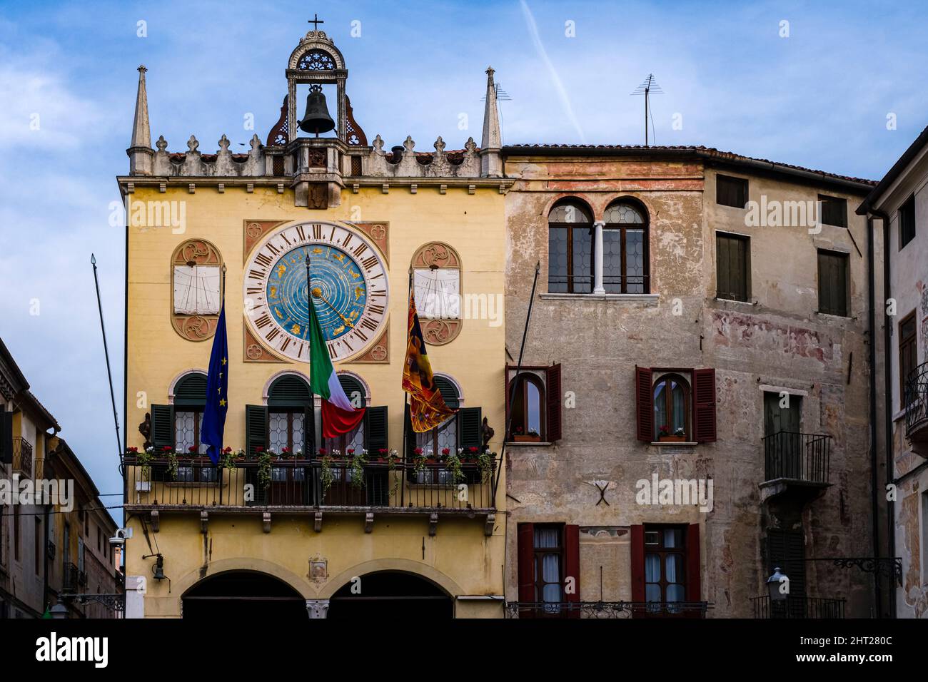 Fachadas de casas medievales de Bassano del Grappa con balcones, un reloj de sol, pequeña torre de reloj y banderas. Foto de stock