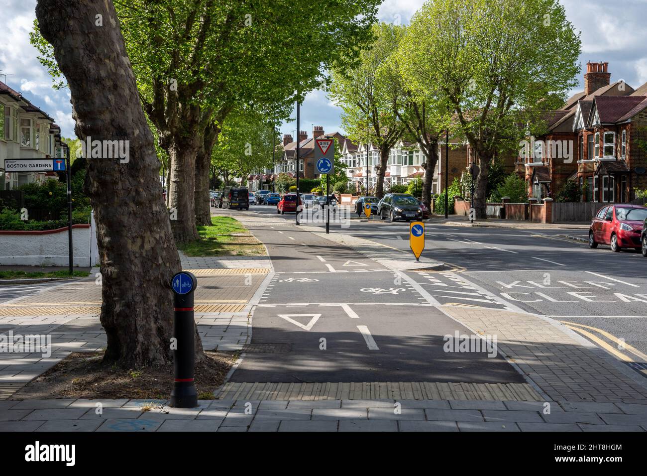 Una pista de ciclismo protegida cruza una calle lateral en una carretera residencial en la periferia del oeste de Londres. Foto de stock