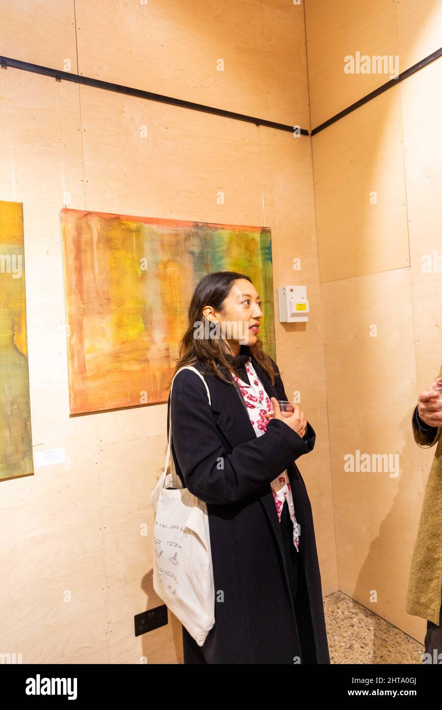 Chica con abrigo negro hablando con alguien una exposición de arte en la apertura en la vibrante Foto de stock