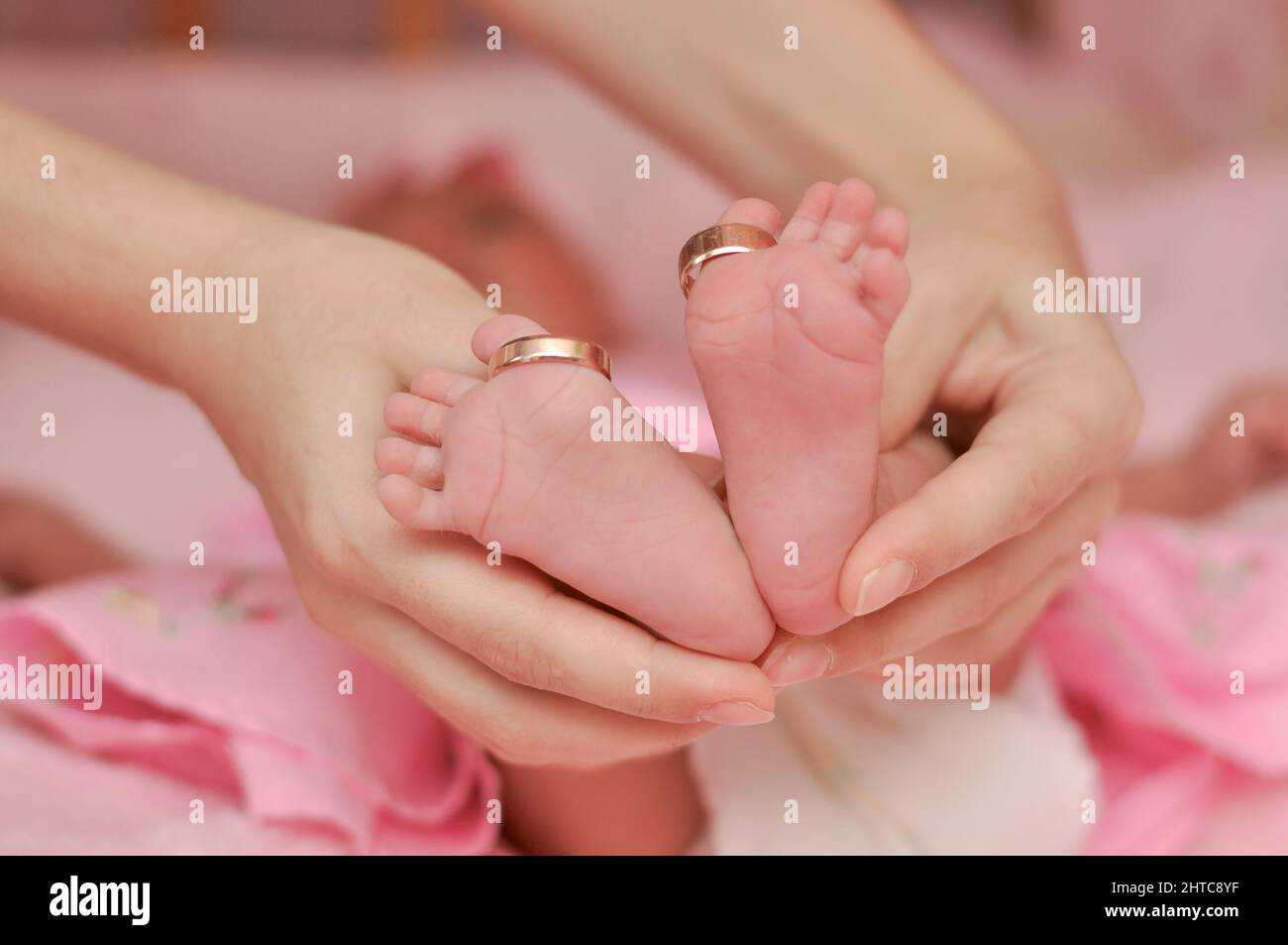 las piernas del bebé están en las manos de la madre. anillos de boda dorados en los dedos de los pies del bebé. concepto de familia o boda Foto de stock