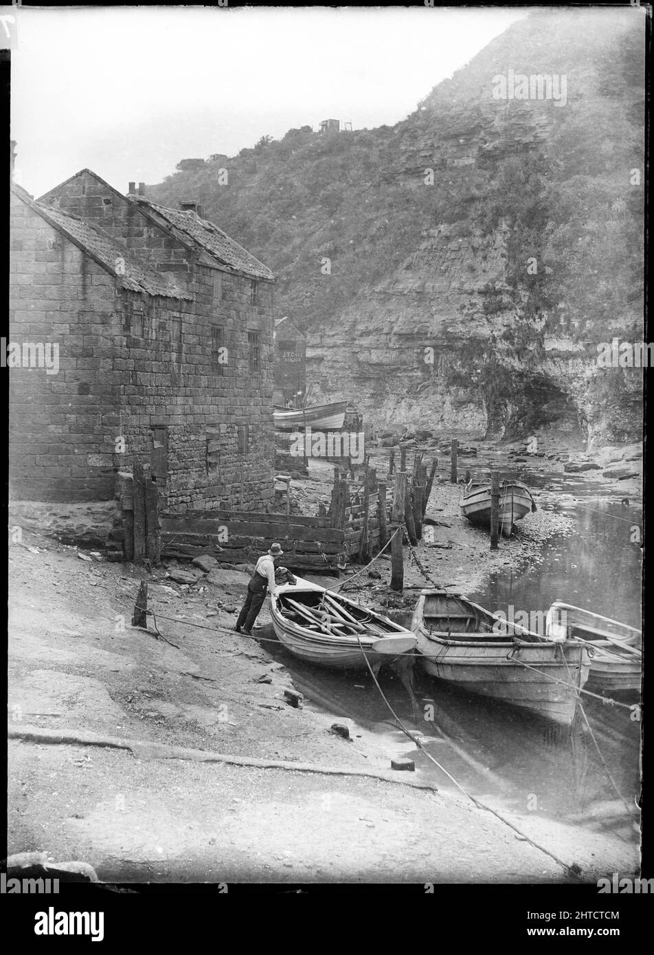 Staithes Beck, Loftus, Redcar y Cleveland, North Yorkshire, 1900-1940. Un hombre de pie junto a un bote de remo amarrado en Staithes Beck. Foto de stock