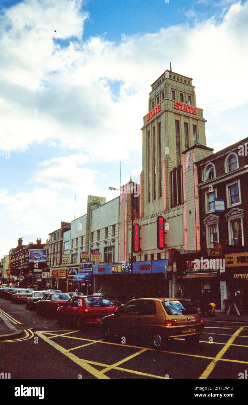 Mecca Bingo Club, Kilburn High Road, Kilburn, Brent, Londres, 1990-2004. El Club de Bingo de La Meca y Kilburn High Road vistos desde el norte. El Teatro Estatal Gaumont fue inaugurado en 1937. Fue uno de los cines más grandes de Europa, y el más grande de Inglaterra, con una capacidad de 4.004 asientos. El diseño exterior se inspira en el Empire State Building de Nueva York. El edificio fue dividido más tarde en una sala de baile, cine y sala de bingo, antes de ser utilizado únicamente como sala de bingo desde alrededor de 1990. En 2010 el edificio se reabrió como una iglesia. Foto de stock