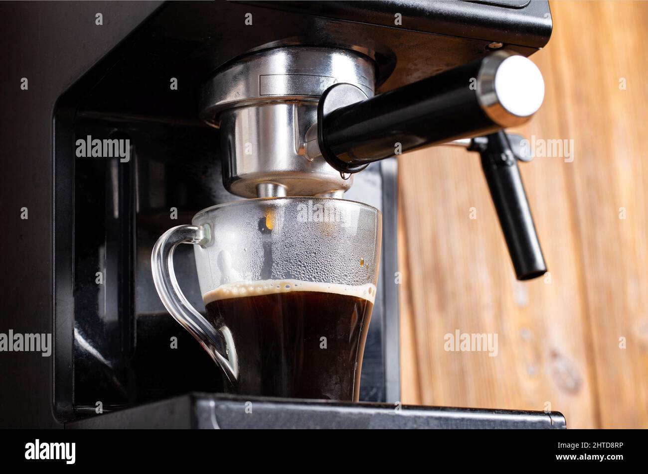 https://c8.alamy.com/compes/2htd8rp/preparar-cafe-en-una-cafetera-en-la-cocina-cerca-cafe-negro-que-fluye-en-una-taza-transparente-sobre-un-fondo-de-mesa-de-madera-cafeina-2htd8rp.jpg