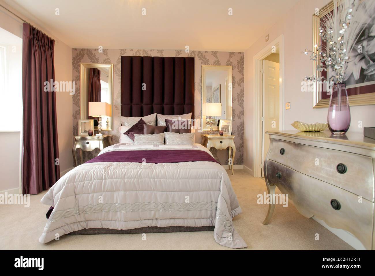 Dormitorio moderno en casa de nueva construcción, colcha, color rojo intenso púrpura borgoña, alto acolchado con cabecera, tocador de plata. Foto de stock
