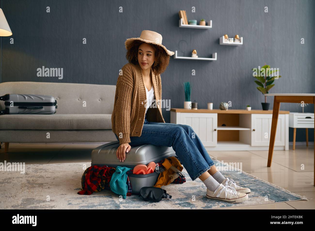 Mujer sentada en la maleta con ropa en exceso Foto de stock