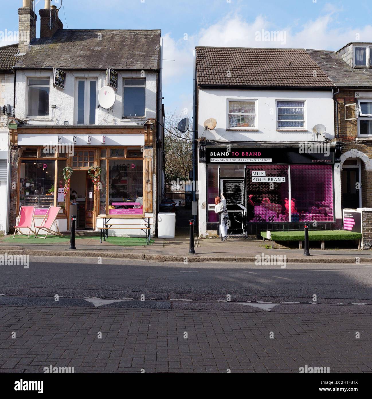 Watford, Hertfordshire, Inglaterra, febrero de 12 2022: Asistente de tienda Red Head con delantal Outside Mood y Bland a las tiendas de marca de colores. Foto de stock