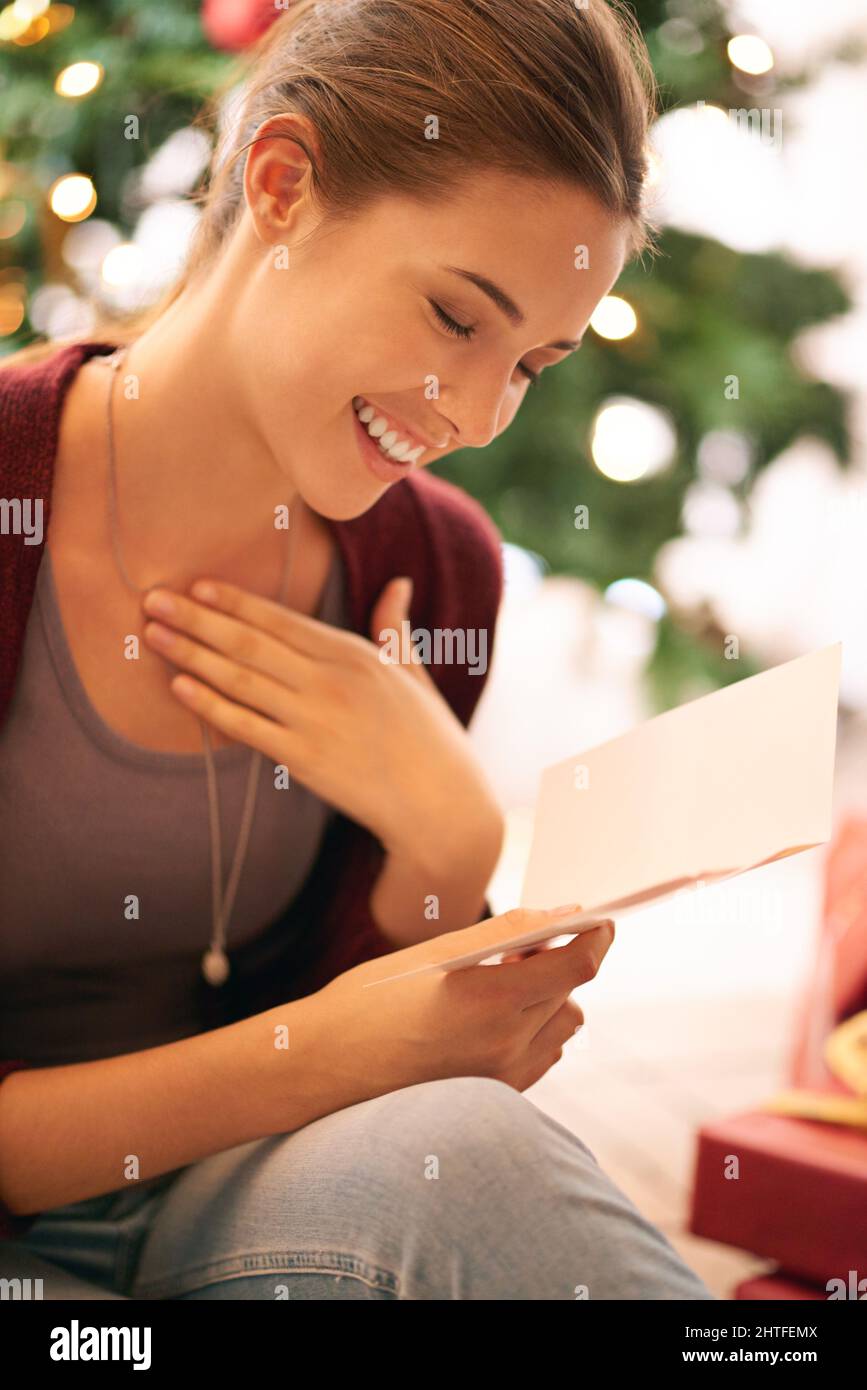 Disfrutar de un mensaje de Navidad sincero. Tiro de una mujer joven hermosa leyendo una tarjeta de Navidad delante de un árbol de Navidad. Foto de stock