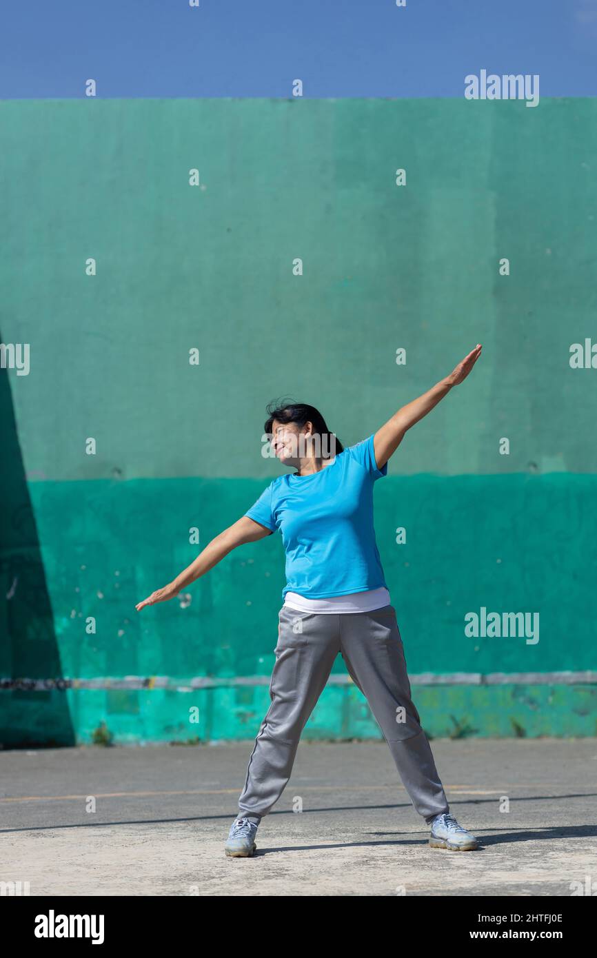 Mujer latina estirando con los brazos extendidos; ejercitando al aire libre Foto de stock