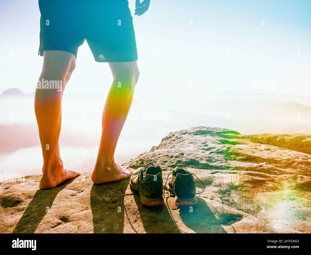 Hombre corredor pies pelados piernas y sudorosos de running y pico rocoso. Misty mañana montañas. Iluminación abstracta, llamaradas coloridas. Foto de stock