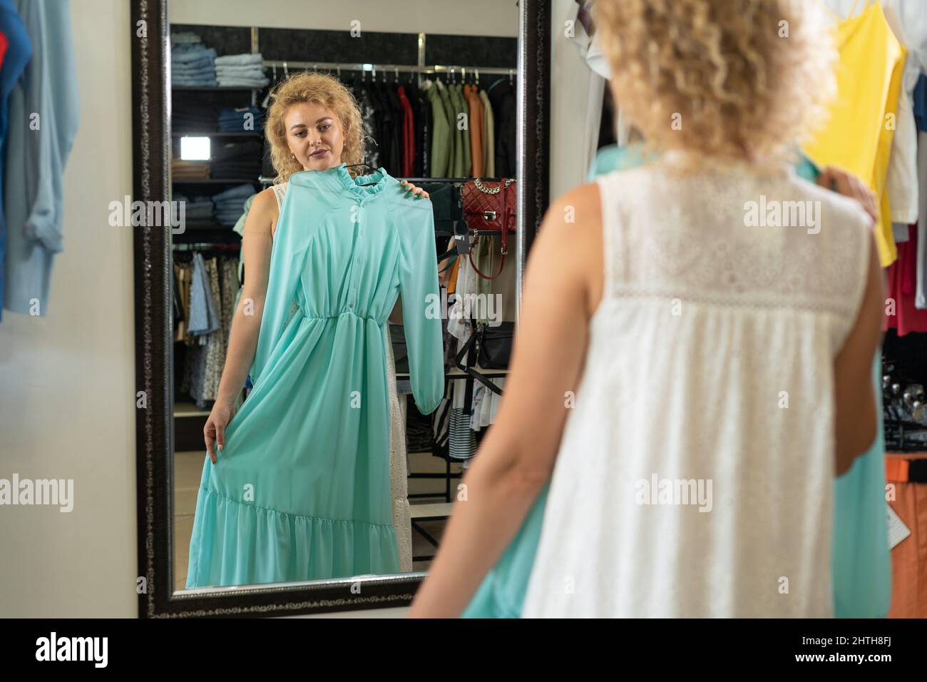 Mujer tratando vestir frente al espejo en la boutique, habitación de ajuste en la tienda de ropa, el departamento de ropa para del centro comercial, chica escogiendo summe Fotografía de