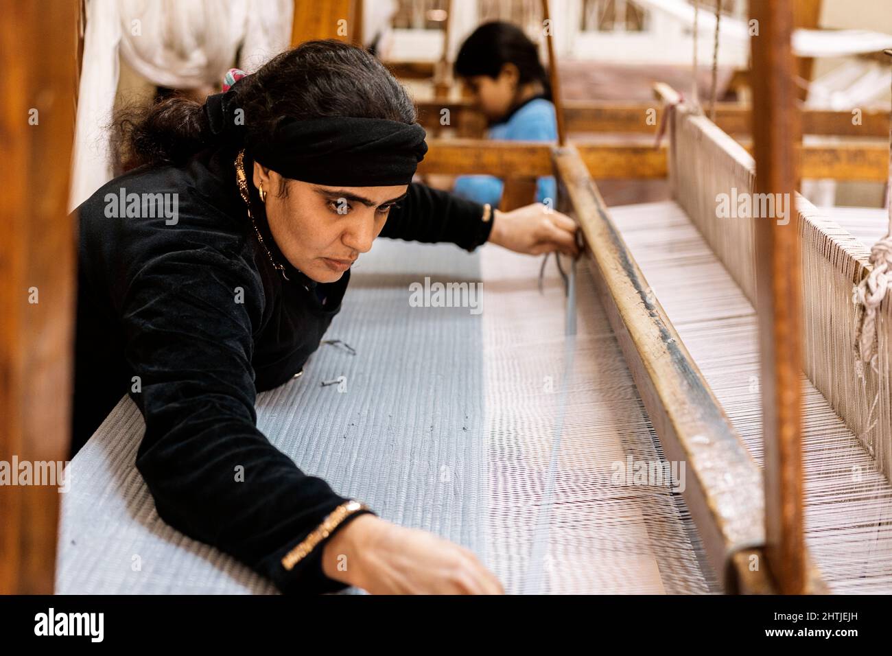 Kairo, Egipto - 12 de enero de 2022: Vista lateral de Zabbaleen concentrada en ropa musulmana tradicional tejiendo tela tradicional por hannd en la Ciudad de la Garb Foto de stock