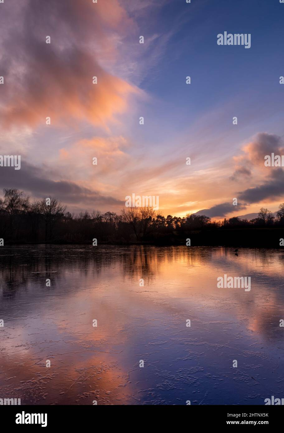 Puesta de sol en el cielo de colores sobre un lago congelado. Bulwell Hall Park Nottingham Inglaterra Reino Unido Foto de stock