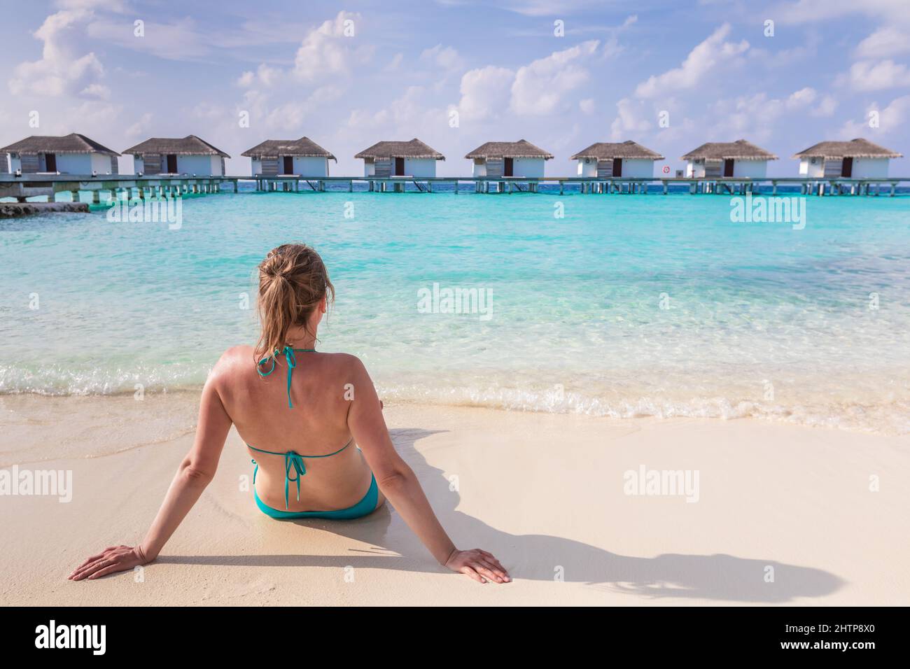 Vacaciones en la playa con mujer sol bañándose en arena blanca en un lujoso hotel resort en Maldivas con villas sobre el agua, aguas turquesas y azul Foto de stock