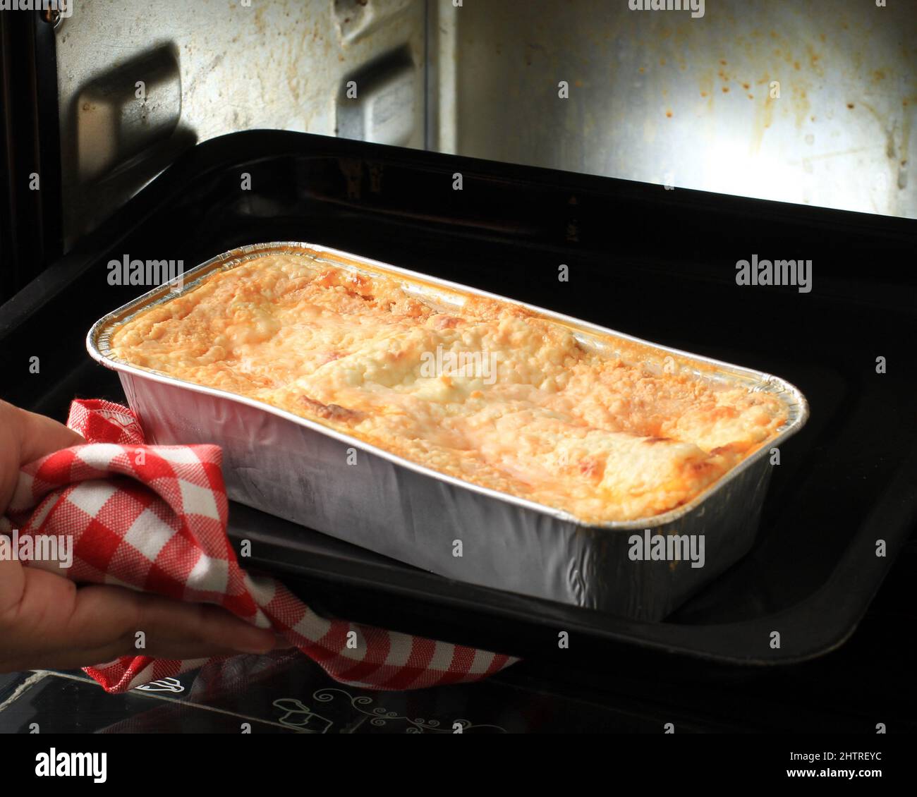 Manos de la mujer Tomando la bandeja para hornear con lasaña fuera del horno  usando la lámina desechable en el horno eléctrico, paso a paso el horno  casero Fotografía de stock -