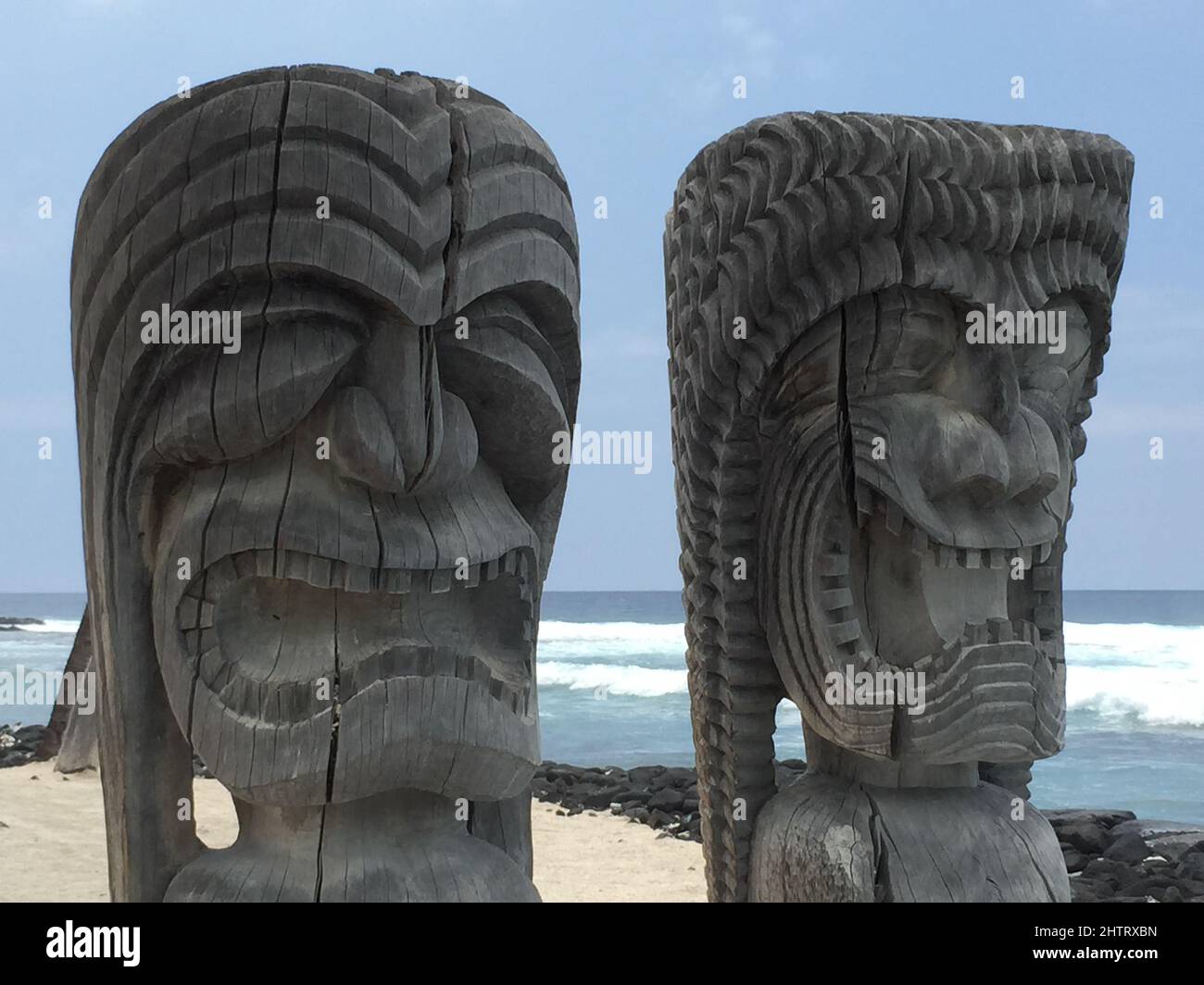 Primer plano de los Tikis hawaianos con expresiones amenazadoras para asustar a los espíritus malignos en la orilla del mar Foto de stock