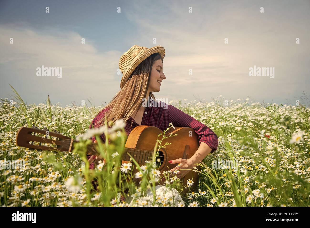 Muy feliz. Hermosa mujer toca la guitarra entre camomila flor campo. Verano  o primavera naturaleza. La belleza estacional. Niña en sombrero jugar  música country en Fotografía de stock - Alamy