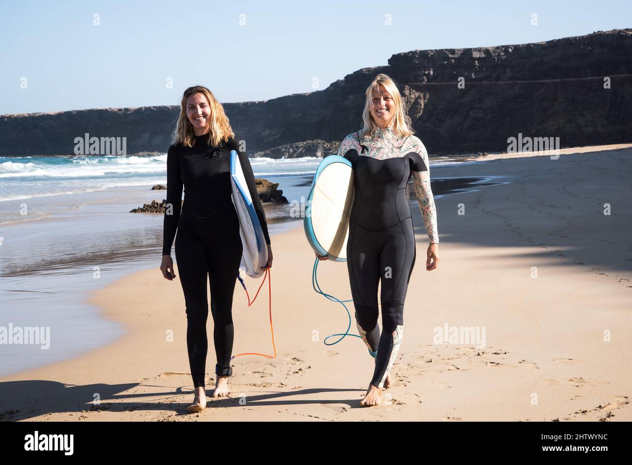 Surfer hembras caminando en la orilla de la playa. Están sonriendo y sosteniendo sus tablas de surf. Foto de stock