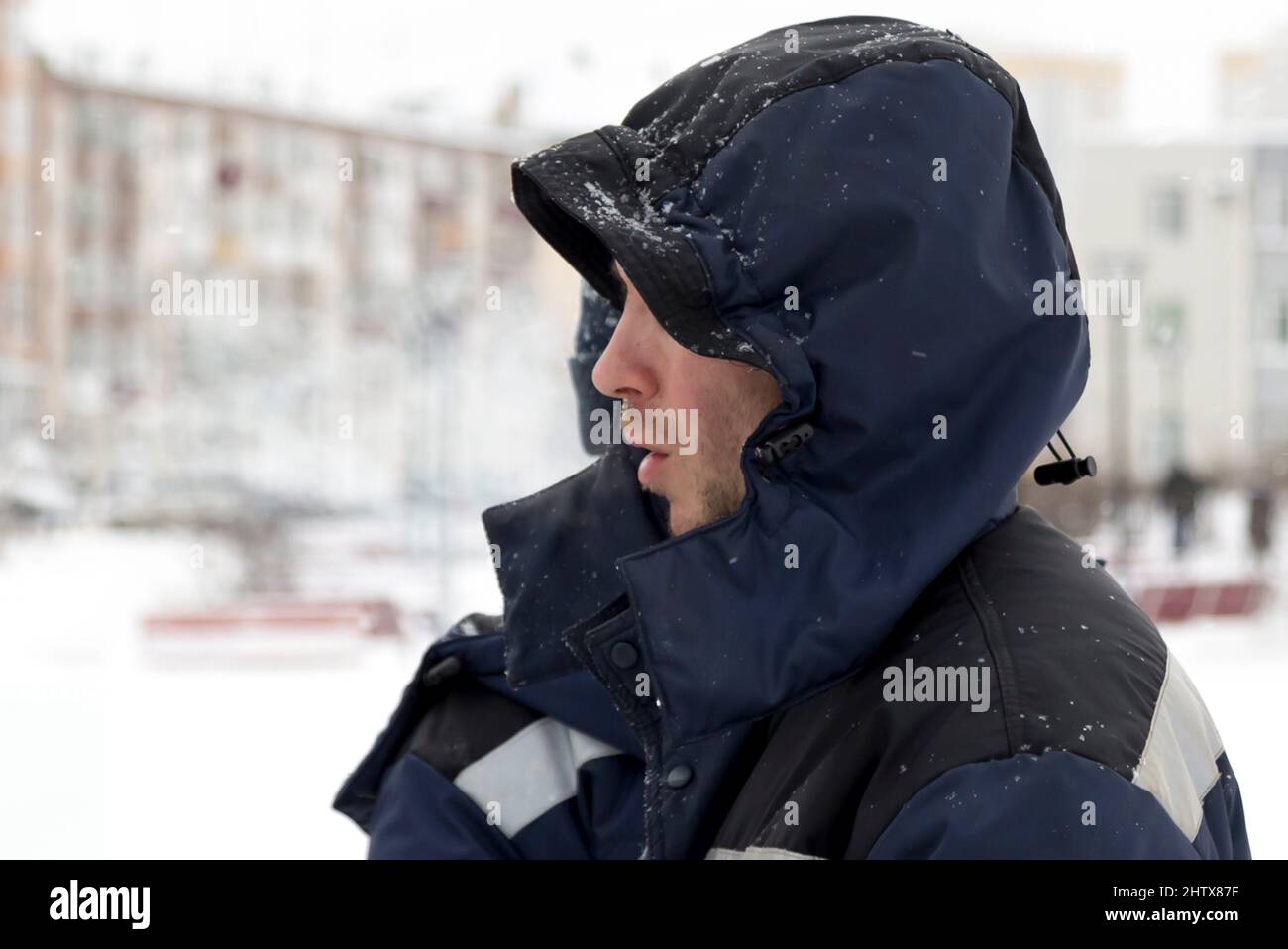 Retrato de un trabajador en una chaqueta con capucha azul en perfil en el lugar de construcción de la ciudad de hielo Foto de stock