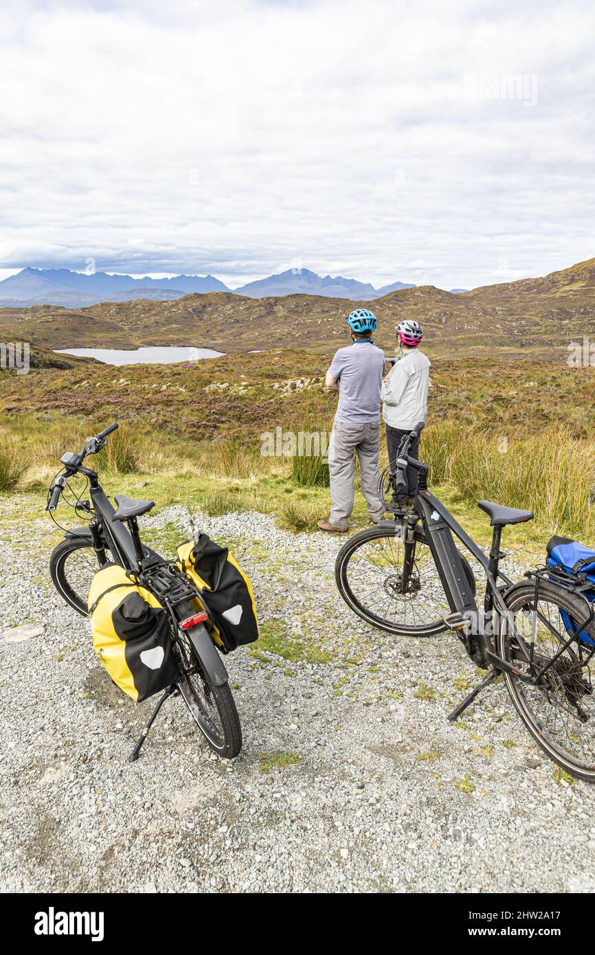 Dos ciclistas en bicicleta eléctrica mirando hacia el norte sobre el lago Dhughaill en la península de Sleat en el sur de la isla de Skye, Highland, Escocia Reino Unido Foto de stock