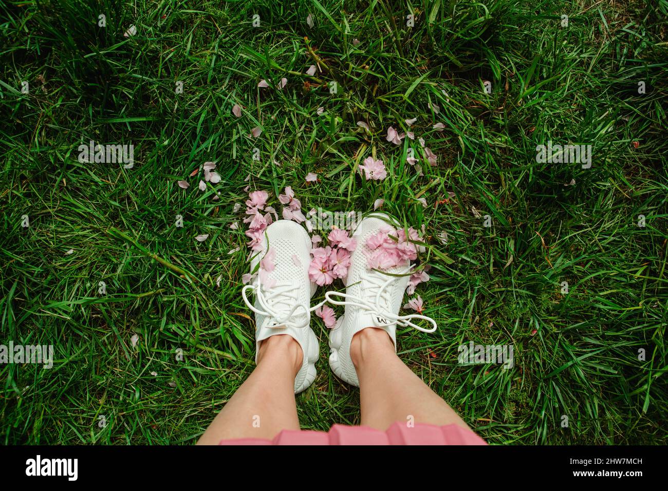 zapatillas de lona de color blanco sobre hierba verde con flores sakura de color  rosa en el espacio de copia Fotografía de stock - Alamy