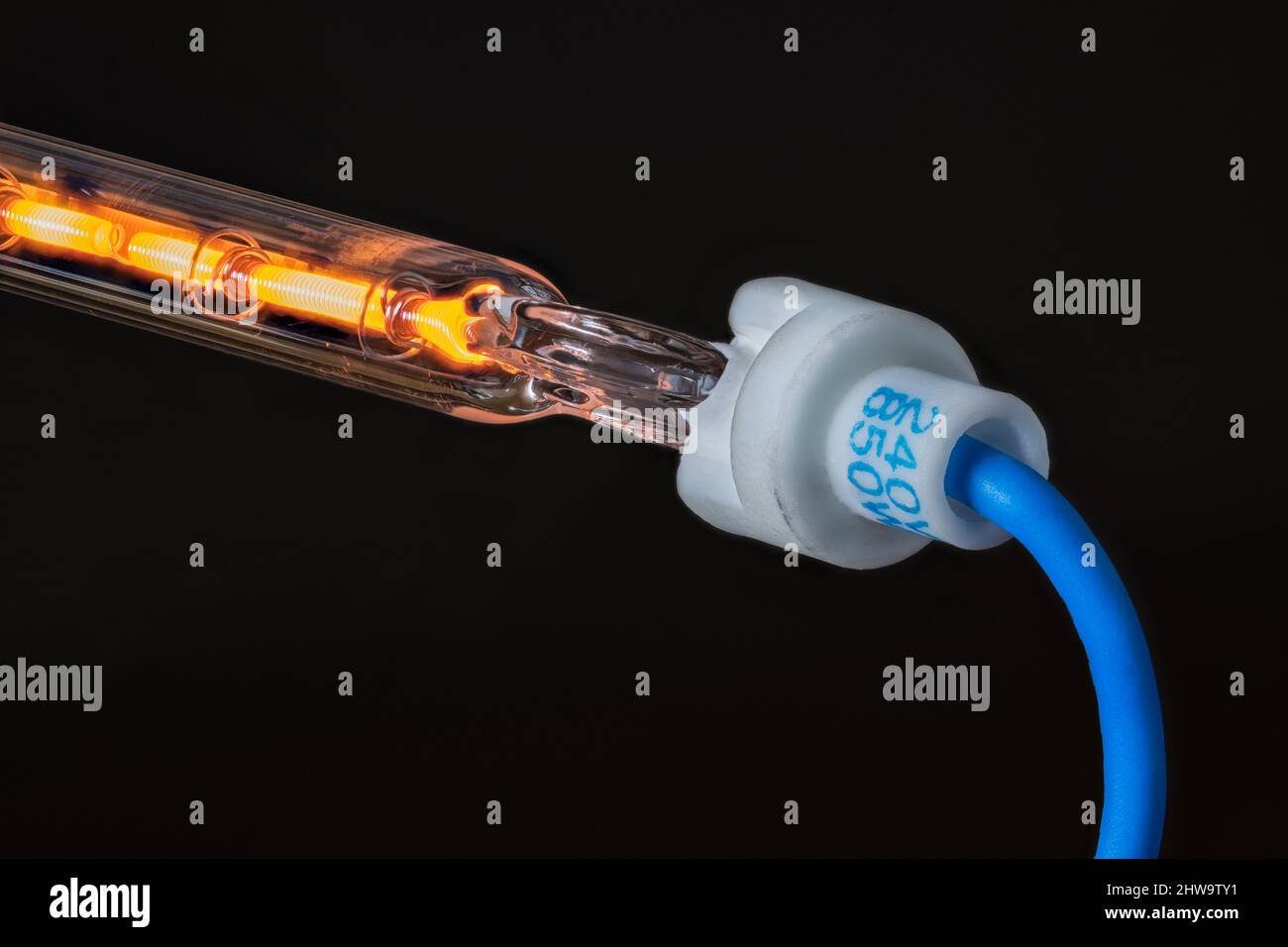 Detalle del cable de resistencia caliente en tubo hueco de vidrio con cable azul sobre fondo negro. Flujo de corriente eléctrica a través del conductor metálico enrollado. Foto de stock