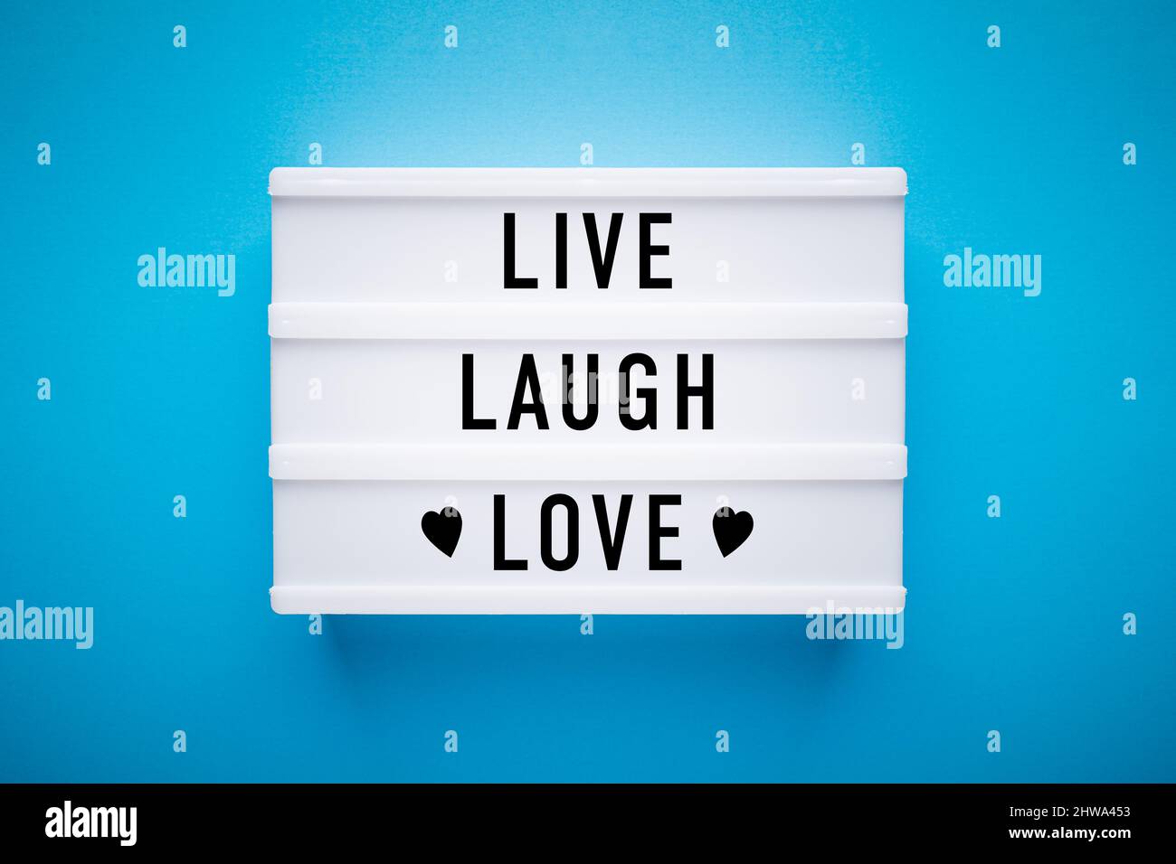 Caja de luz sobre un fondo azul claro con mensaje en él: Vivir, reír, amar. Foto de stock