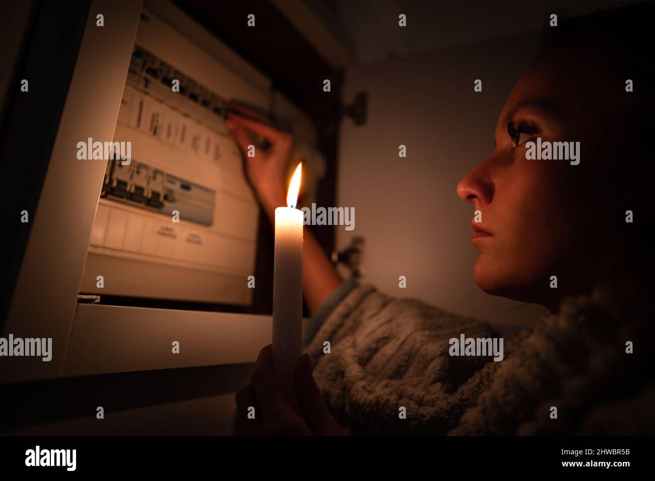 Mujer comprobando la caja de fusibles en casa durante un corte de corriente o apagón. No hay concepto de electricidad Foto de stock