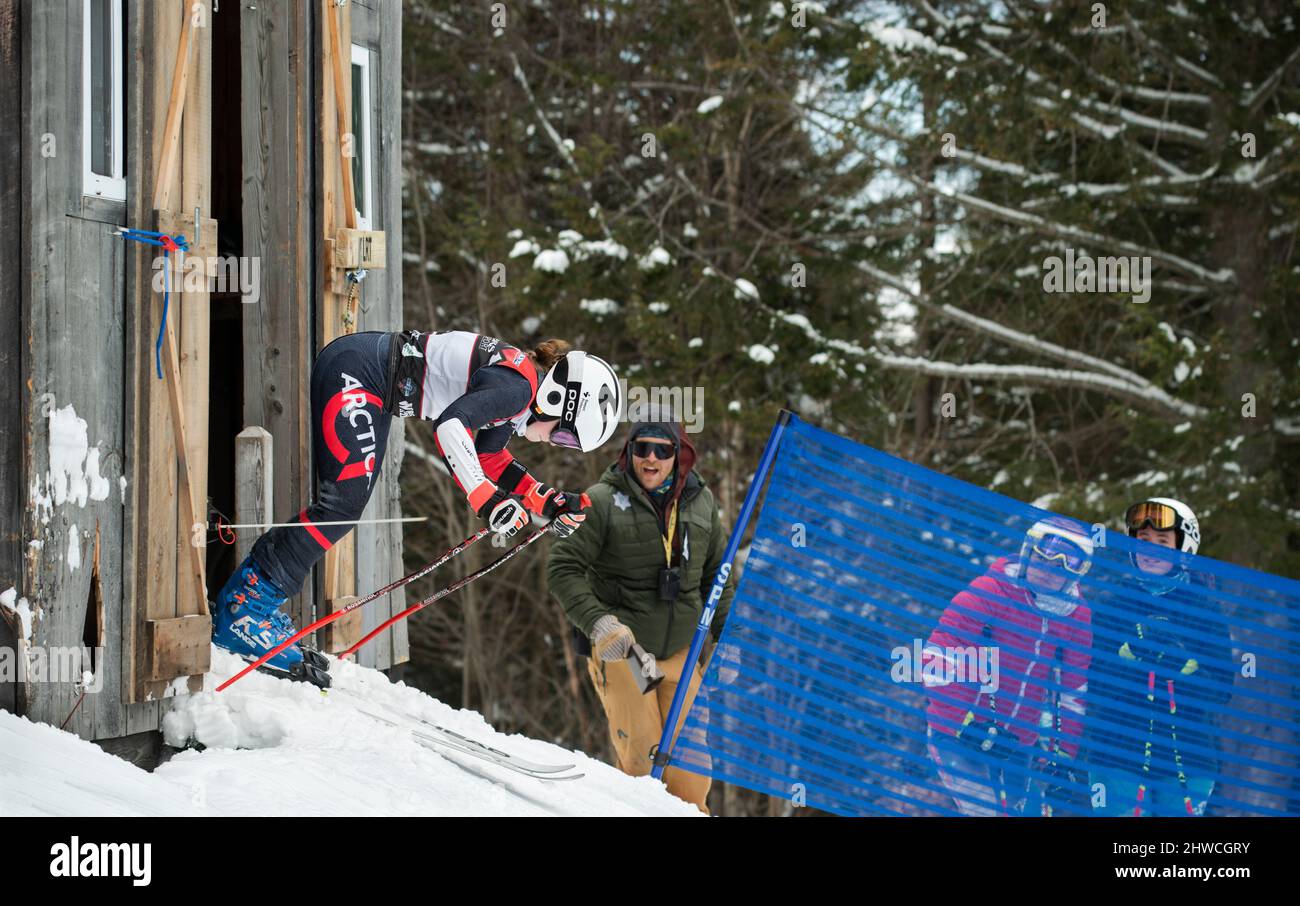 Puerta de salida durante el slalom gigante 2022, Lafoley New Hampshire Alpine Racing Association (NHARA) en Loon Mountain, NH. Una racer femenina de U16 sale de la puerta de salida mientras uno de sus entrenadores grita aliento y suena una campana de vaca. Foto de stock