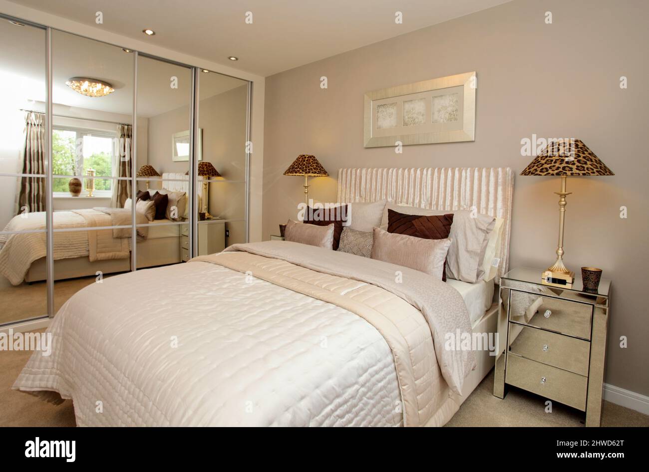 Dormitorio en esquema de colores neutros con armarios de espejo, colcha de cama en moderno showhome. Foto de stock