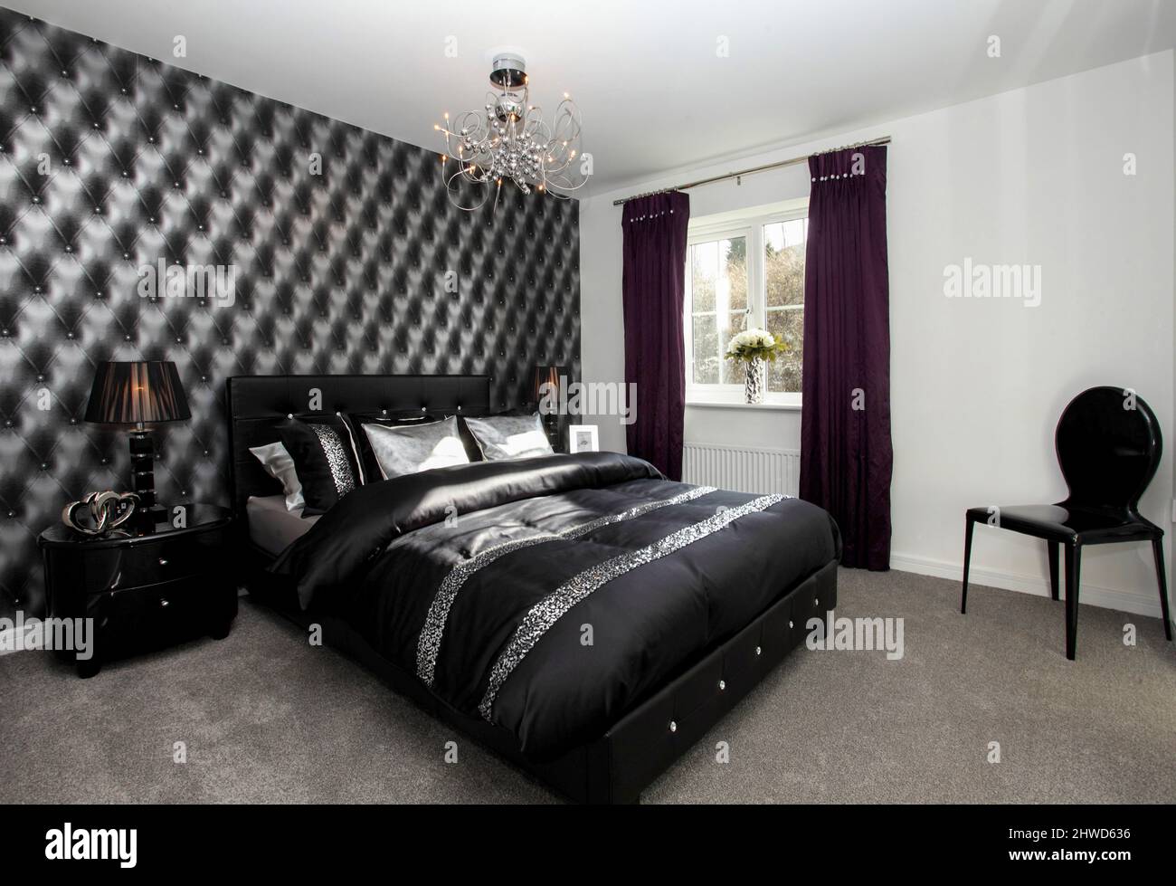 Dormitorio blanco y negro dramático, papel pintado en efecto acolchado negro, sábanas satinadas negras almohadas. Foto de stock