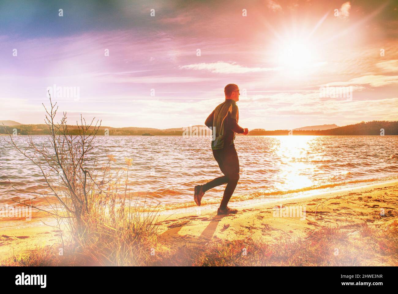 Hombre alto que huida solo del lago. El hombre corre en la playa. Iluminación abstracta, llamaradas coloridas. Foto de stock
