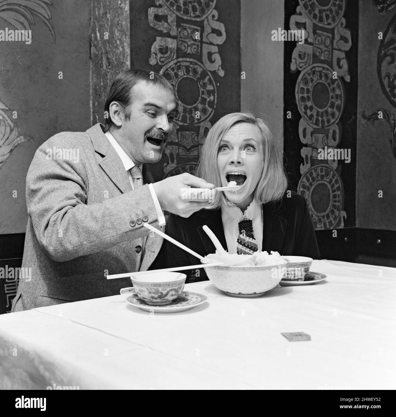 Stanley Baker, que aprendió el arte de comer con palillos en restaurantes chinos en Liverpool, muestra a Blackman honor lo fácil que es. La pareja comenzará a filmar pronto la producción de Josef Shaftel 'Grisby' en Hong Kong. 31st de marzo de 1969. Foto de stock