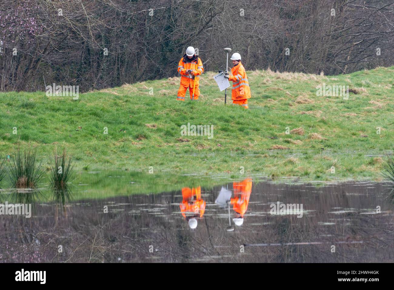 Dos trabajadores en ropa de alta visibilidad que examinan la extensión y la causa de las inundaciones en un parque rural, Hampshire, Inglaterra, Reino Unido Foto de stock