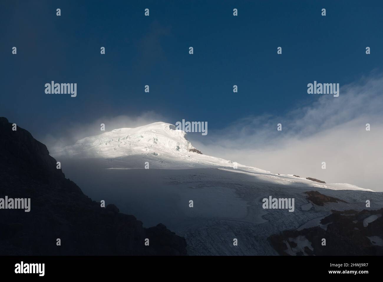 Pico y glaciar del volcán Cayambe al atardecer con niebla, Parque Nacional Cayambe Coca, Ecuador. Foto de stock