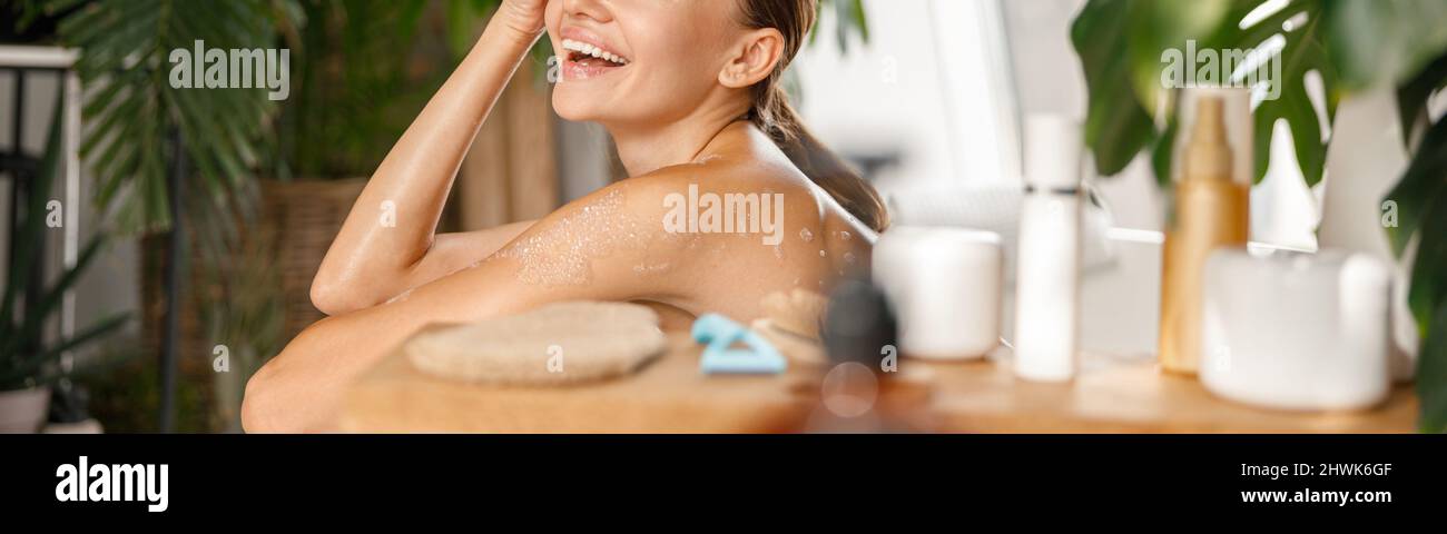 Alegre joven sonriendo lejos mientras que baña y cuida de su cuerpo en balneario tropical Foto de stock