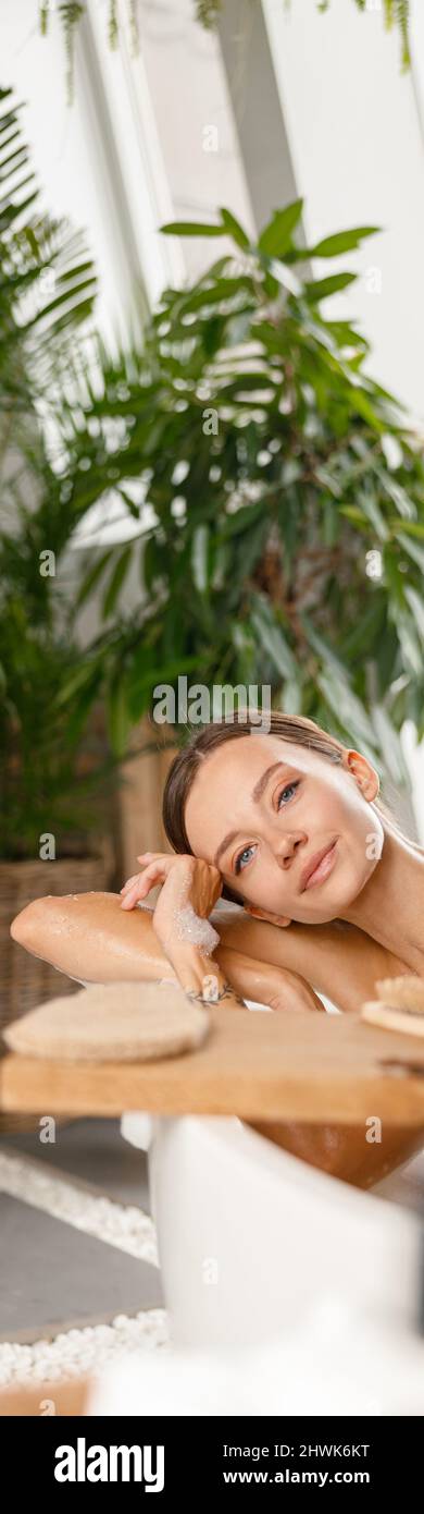 Una mujer joven y tranquila mirando la cámara mientras se toma un baño de burbujas en un spa tropical Foto de stock