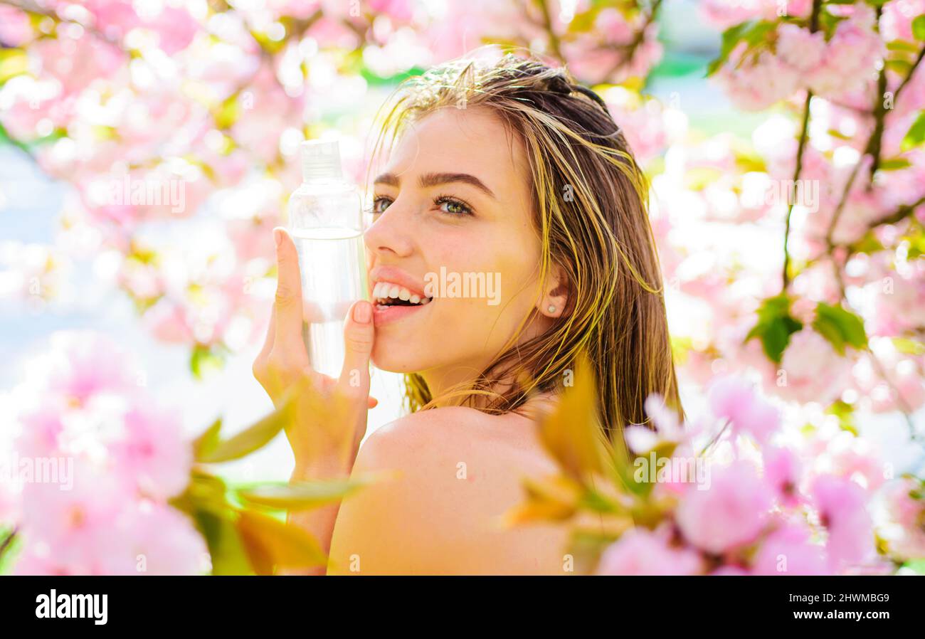 Chica con botella de tónico cosmético. Mujer sonriente con agua micellar. Limpieza del tóner para limpiar la piel. Foto de stock
