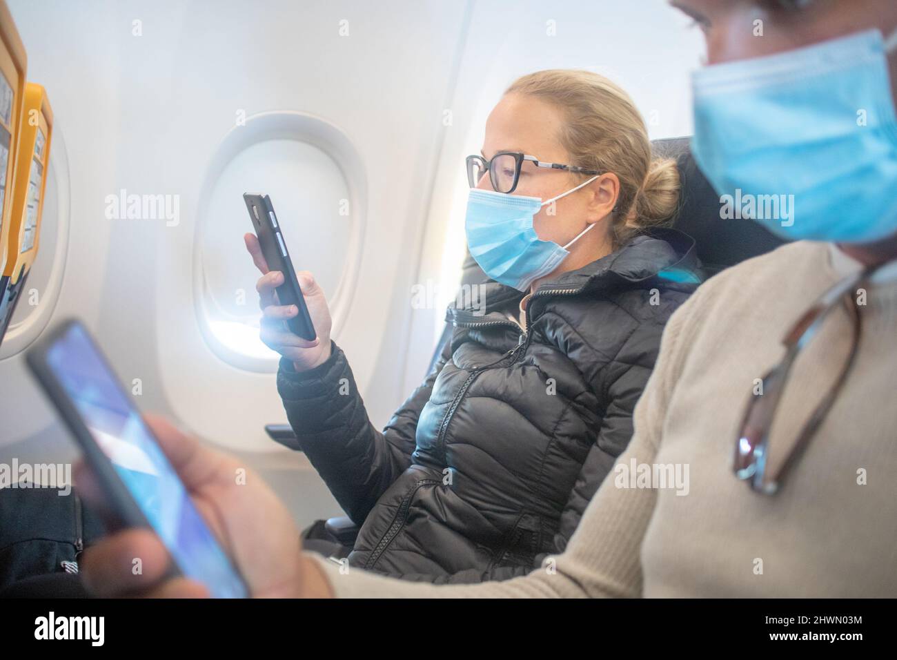 Una pareja joven con mascarilla, usando un teléfono inteligente mientras viaja en avión. Nuevo viaje normal después del concepto de pandemia de covid-19. Foto de stock