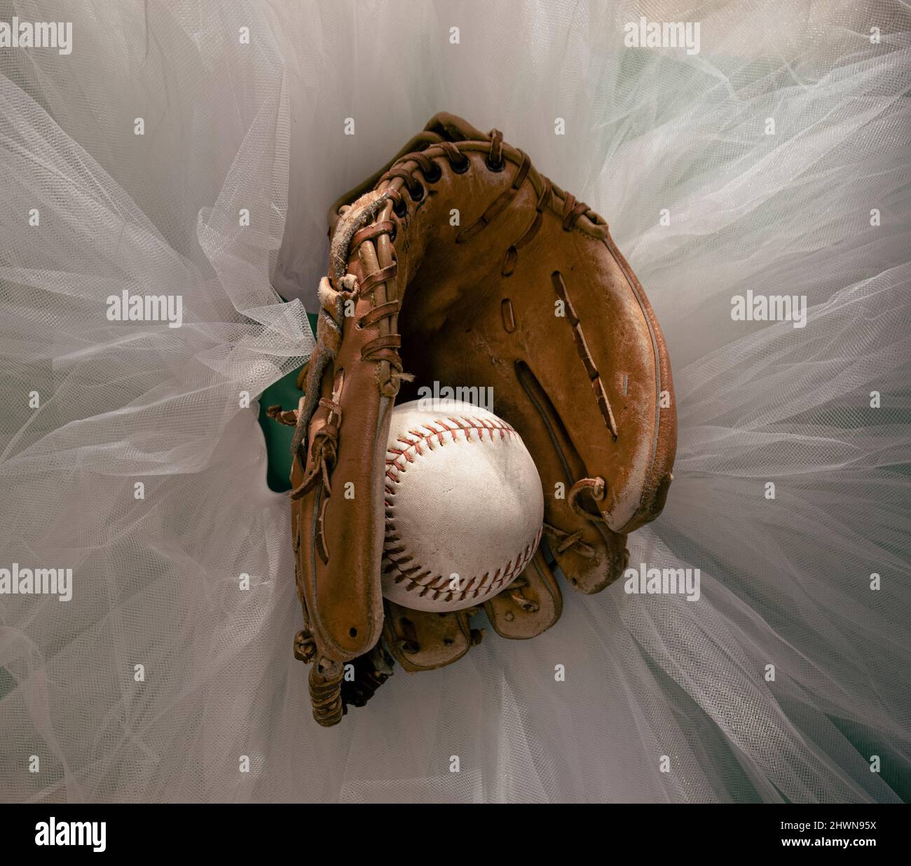 Guante de béisbol con softbol a mitad, sentado en la parte superior de un tutu de ballet blanco. Foto de stock