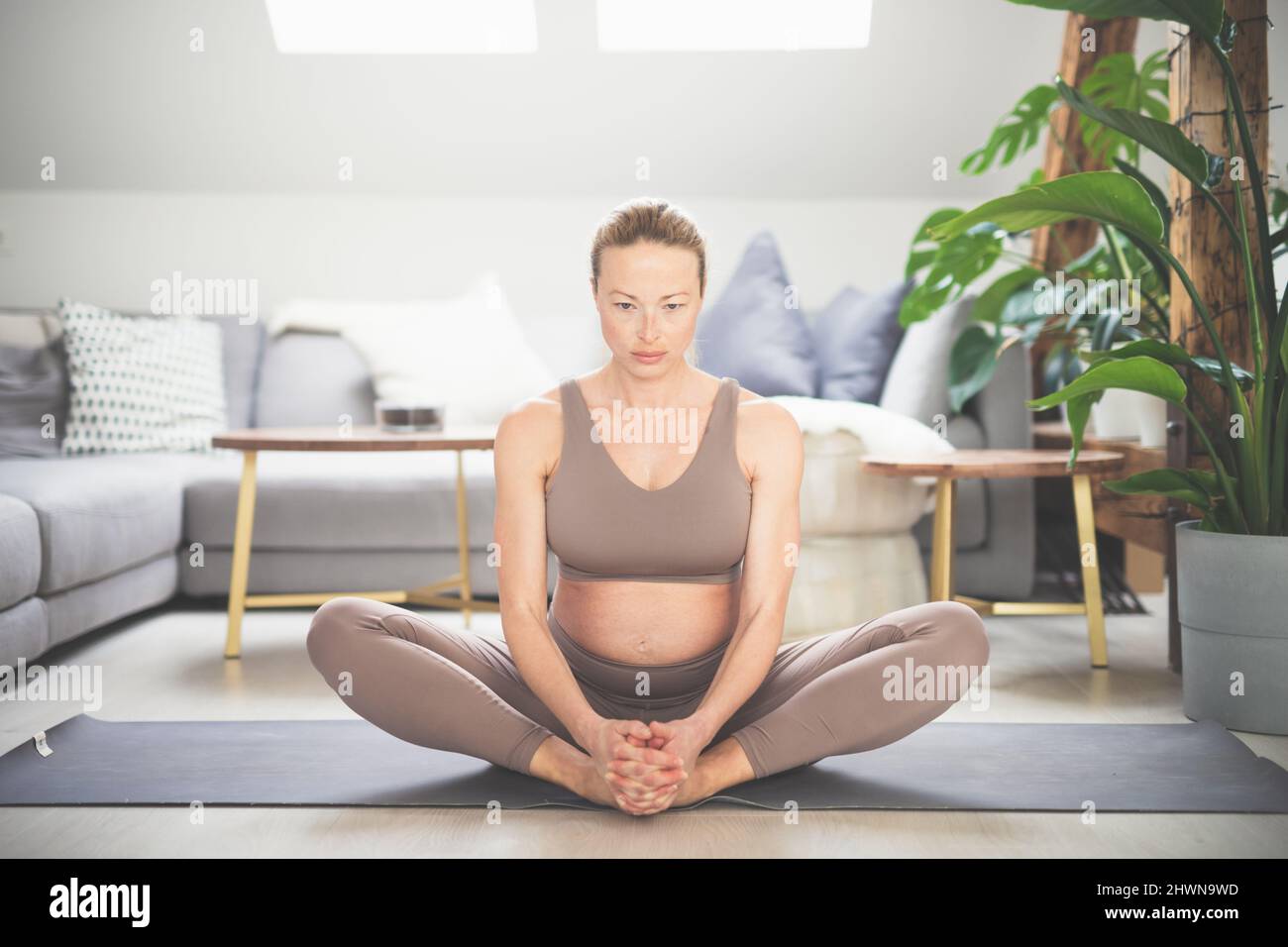 Joven hermosa mujer embarazada practicando yoga en casa en su salón. Maternidad, embarazo, estilo de vida saludable, bienestar y concepto de yoga. Foto de stock