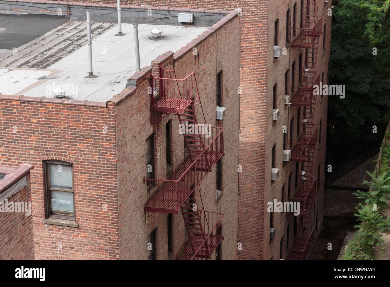 parte de atrás de edificios de apartamentos de ladrillo rojo de aspecto genérico sin descripción, con escapes de incendio y unidades de aire acondicionado de ventana Foto de stock