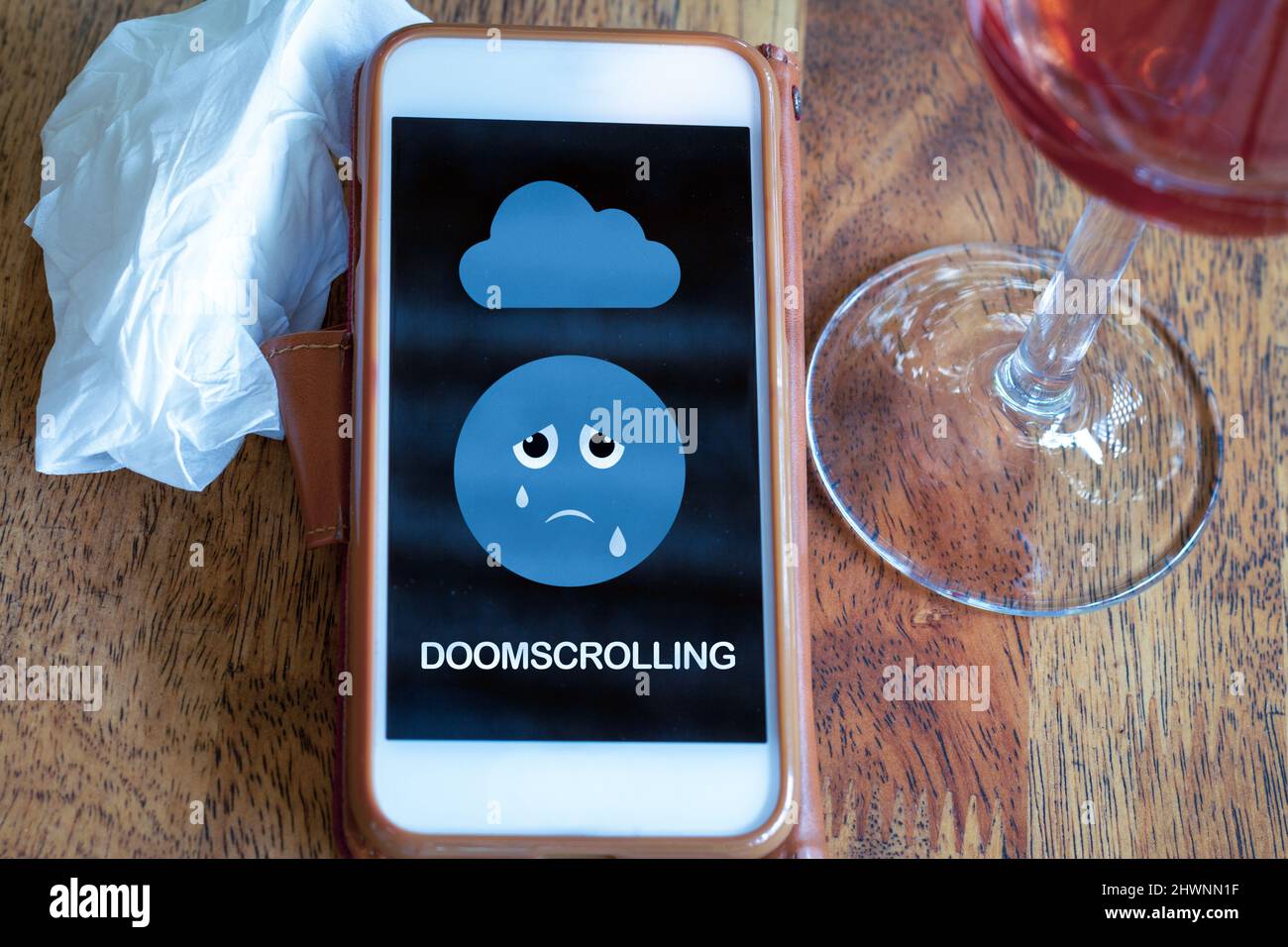 Doomscrolling en el teléfono móvil sobre la mesa con una copa de vino y tejidos, continuando la búsqueda o el desplazamiento a través de las malas noticias y eventos en las redes sociales, incluso Foto de stock